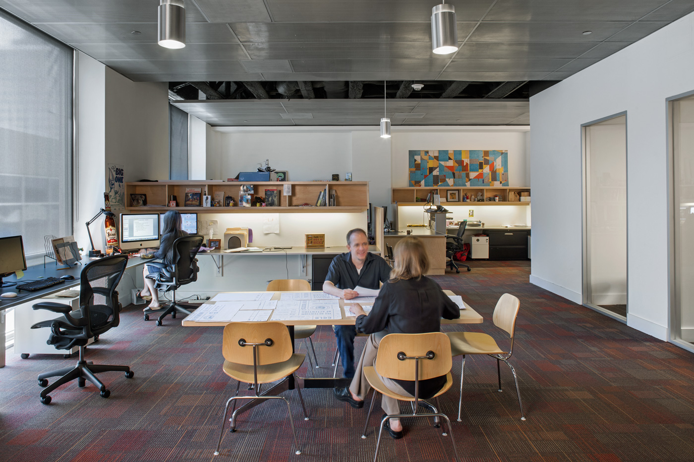 Two coworkers talking at large central work desk.